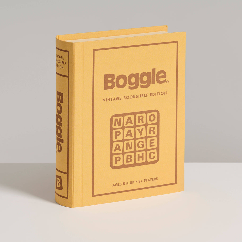 A yellow, book-shaped box of Board Game: Boggle Vintage Bookshelf Edition stands upright on a white surface, showing the classic word game grid and labeling it for ages 8+ and two or more players.
