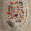 Detailed embroidery of animals and plants adorns the Sugar Egg Pocket Pillow, depicting a lamb, rabbit, duck, and fox among mushrooms and flowers. Earthy tones with pops of red, orange, and purple are enhanced by a metallic gold leaf border featuring an embroidered lamb at the bottom.