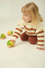 A young child with blonde hair, wearing a cream and brown striped sweater and brown pants, kneels on the floor while playing with Lou The Lemon Baby Car—an eco-friendly sensory toy made from natural rubber and shaped like a lemon.