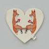 Embroidered Coral & Tusk Smitten Foxes Felt Envelope depicting two orange foxes sitting on a bench, each holding a pink heart, set against a light grey background.