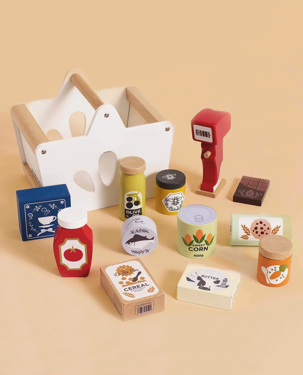 The Groceries Set & Scanner is a colorful wooden playset with toy groceries—boxes, jars, cans, ketchup bottle, chocolate bar—a red barcode scanner and white basket, perfect for pretend shopping in any toy kitchen on a beige background.