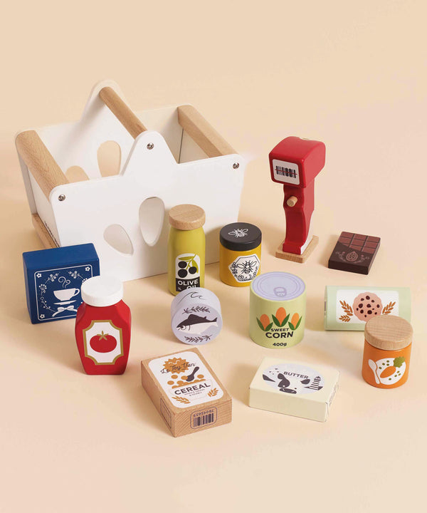 The Groceries Set & Scanner features a white basket, jars, cans, ketchup bottle, chocolate bar, cereal box, and red scanner. Ideal for pretend shopping play and imaginative fun! All items pictured on a beige background.