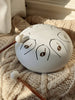 A Steel Tongue Drum in white, labeled with musical notes, sits on a knitted beige blanket beside two wooden mallets—an elegant musical toy instrument in soft sunlight.