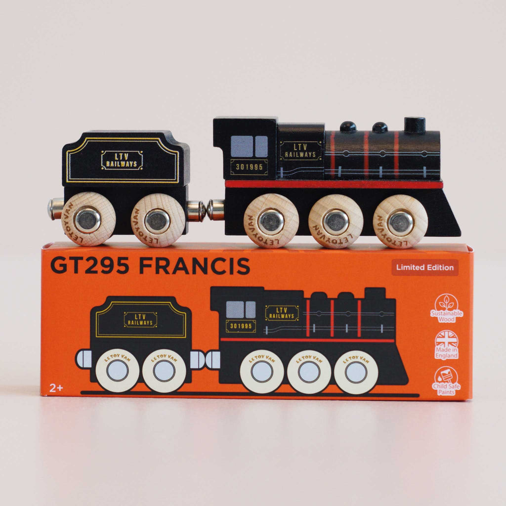 A wooden toy train and coal car rest atop an orange box labeled “No. 49 GT295 Francis | Made in England.” Evoking the charm of classic locomotives, both the train and the box showcase coordinated black, gold, and red designs, with “LTV RAILWAYS” displayed on each train piece.