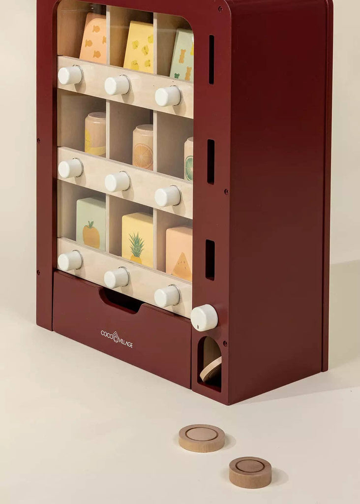 The Wooden Play Vending Machine features a burgundy frame, white knobs, and illustrated wooden fruit and cheese blocks. With two wooden coins included, this pretend play toy helps develop motor skills.