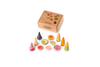A cardboard box labeled "Veggies" sits behind the Grapat Play Set - Veggies: colorful wooden vegetables for pretend play, featuring sliceable and whole carrots, tomatoes, cucumbers, and figs arranged on a white surface.