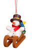 The Christian Ulbricht Ornament - Snowman on Sled features a snowman with a red scarf and brown hat, holding a green tree on a wooden sled, a blue and yellow bird on its arm, and hangs by a red string. Fine German craftsmanship.