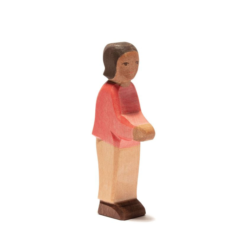 A wooden figurine of a person with short brown hair stands upright. The figure is dressed in a red shirt with beige pants and brown shoes. The simplistic design features smooth contours and minimal facial details, embodying the charm of handcrafted wooden toys, much like the Ostheimer Son, Red Sweater.