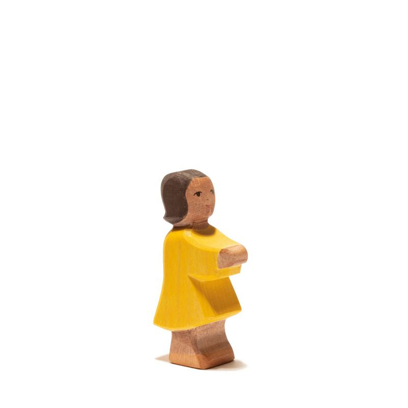 A handcrafted wooden figurine of a person with brown hair wearing a yellow dress. The figure's arms are crossed in front, and it stands on a plain white background, perfect for imaginative play and seamlessly fitting into any Ostheimer Daughter collection.