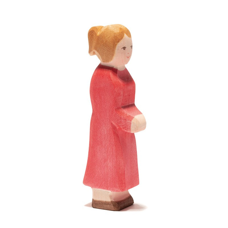 An Ostheimer Mother, Red Dress, figurine of a woman with blonde hair tied in a bun, wearing a long red dress, stands in profile. Crafted from sustainably sourced materials, the figure has minimal facial features and simplified details, embodying the essence of handcrafted wooden toys.