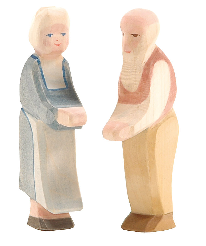 A wooden figurine set featuring two elderly people, meticulously handcrafted from maple. One is an old woman wearing a gray dress with white hair and rosy cheeks, while the other is an Ostheimer Grandfather with a bald head, white beard, and wearing a brown shirt and beige pants. Perfect for Ostheimer collectors.