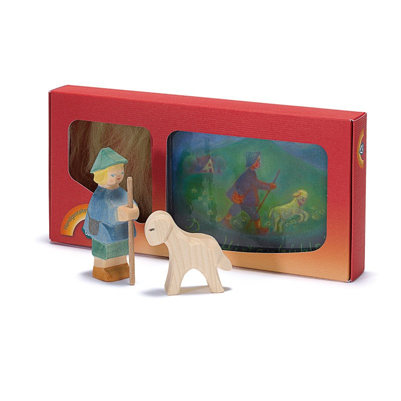 The Ostheimer The Shepherd Boy Book Set features a small shepherd figure with staff and a wooden sheep, placed before a red box with an illustrated scene—ideal for inspiring imaginative play.