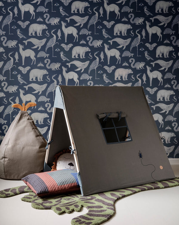 A cozy children's play area with a Ferm Living Tent - Beetle Embroidery - Dark Olive, large bean bag, and a colorful cushion on a green rug, set against a wallpaper featuring a pattern of elephants.