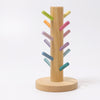 The Grimm's Pastel Sorting Helper for Building Rings is a wooden tree-like structure, crafted from alder wood, standing upright with colorful cylindrical pegs inserted at various angles. The base is circular, and the non-toxic pastel pegs in pink, purple, blue, green, and yellow create a vibrant and playful appearance.