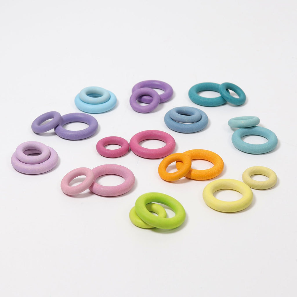 Grimm's Pastel Building Rings, made of colorful silicone in varying sizes and shades such as purple, blue, pink, orange, green, and yellow, are scattered on a white background. Each set features two matching rings designed for stacking and sorting to enhance fine motor skills.