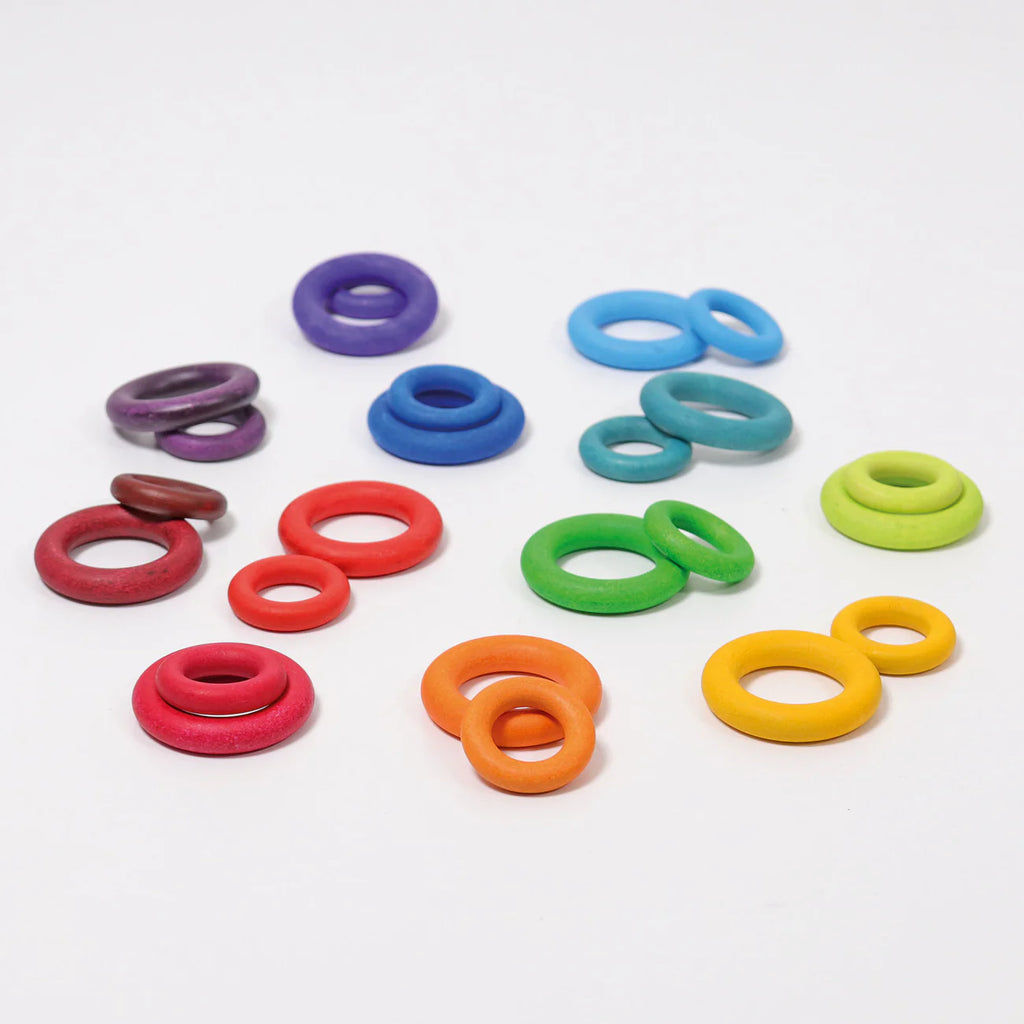 The Grimm's Sorting Helper with Building Rings Set features colorful wooden rings in purple, blue, green, yellow, orange, and red—ideal for developing fine motor skills on a white surface.