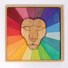 A Grimm's Rainbow Lion Building Set featuring a lion's face at the center, surrounded by colorful geometric shapes in a gradient pattern. The segments radiate outward in a spectrum of rainbow colors from red to purple, all nestled within a natural wood frame.