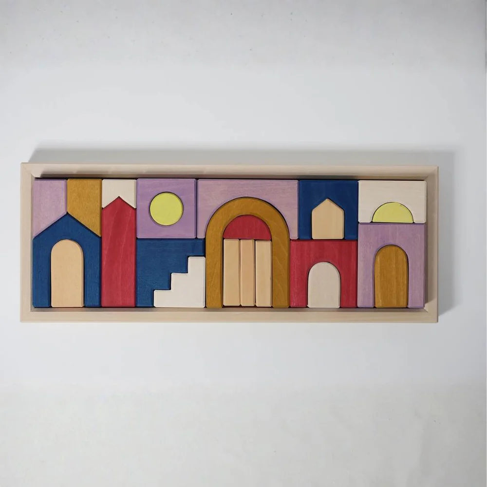 Grimm's Panorama Building Set is a rectangular wooden tray with colorful blocks—red, blue, yellow, brown, and purple—arranged as abstract buildings and arches against a white background. Part of the Tiny Art Collection.