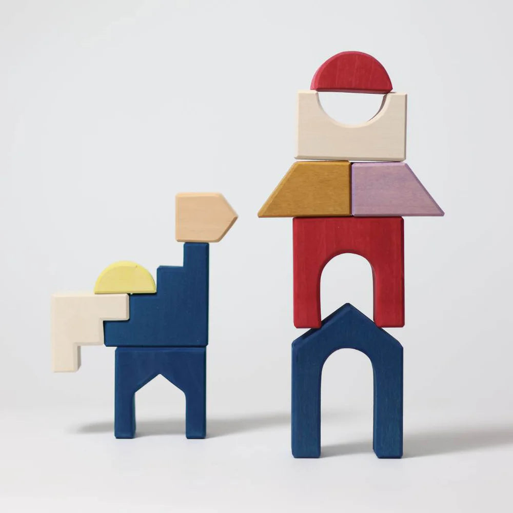 Two vibrant wooden structures from Grimm's Panorama Building Set stand on a plain surface—one animal-like, the other a tall stack of geometric shapes—a striking piece for any TINY ART COLLECTION.