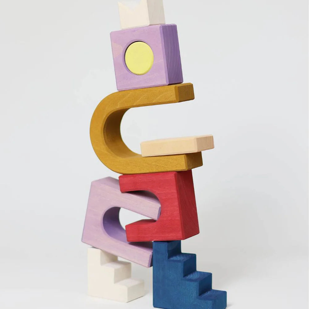 The Grimm's Panorama Building Set features colorful wooden blocks in unique shapes—arches, stairs, and squares—artfully stacked to create imaginative structures against a white background.