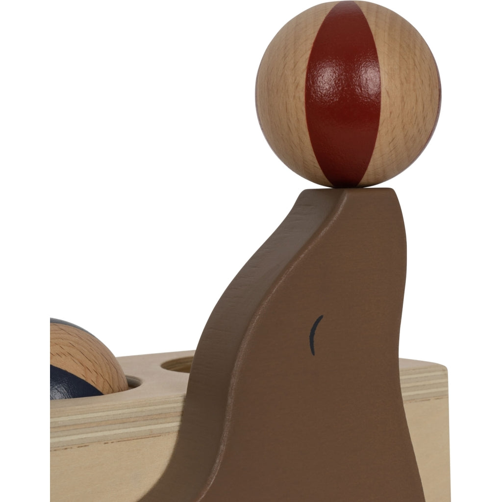 A close-up image of a Wooden Hammer Game - Sea Lion with a smooth, dark brown track and a spherical red and natural wood-colored ball perched on top, crafted from FSC-certified wood.