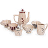 A beige Konges Sløjd Pretend Play Porcelain Tea Set including a teapot with a red lid, four cups, a sugar bowl, and a milk jug, all decorated with simple brown leaf motifs.