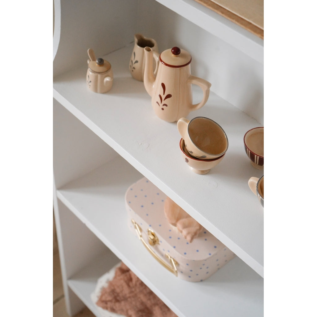 A serene home shelf display featuring a decorative Konges Sløjd Pretend Play Porcelain Tea Set in pastel tones with floral designs, accompanied by a dotted pink box on a white shelving unit.