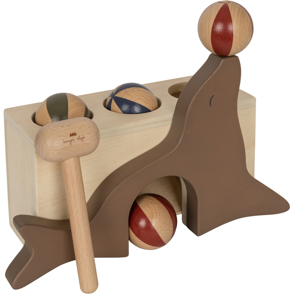 Wooden Hammer Game - Sea Lion with a dinosaur motif, featuring holes for three balls to be pounded through and a mallet, crafted from FSC-certified wood in natural and brown colors.
