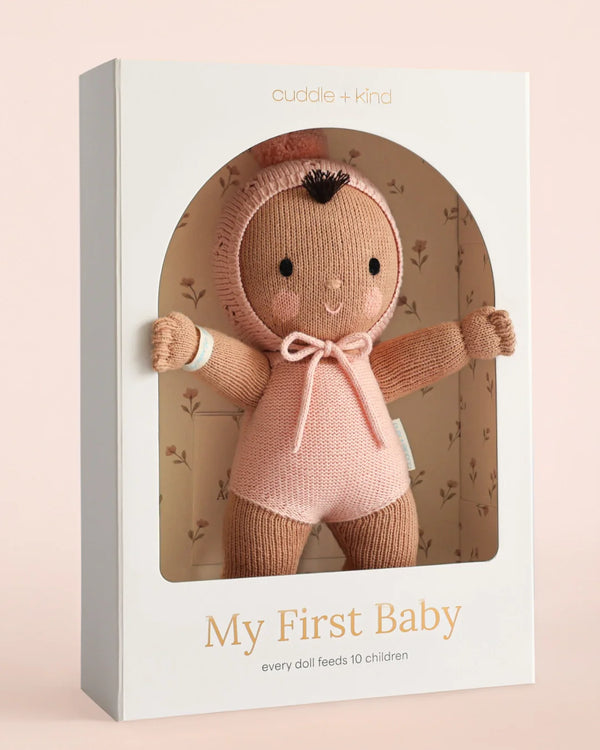 The Cuddle + Kind My First Baby (Peach) doll ships in one week. Made from natural cotton yarn, it features brown skin, a pink knit hooded outfit, and a smiling face. Every purchase helps feed 10 children.