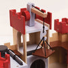 A close-up of the Lionheart Wooden Castle shows its sustainable wooden construction, red battlements, a pulley system, and a platform suspended on black cords that acts as a drawbridge or lift—perfect for inspiring imaginative play.