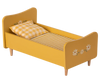 The Maileg Wooden Bed, Mini is a charming toddler bed in yellow, featuring hand-painted floral decorations on both the headboard and footboard. This delightful piece comes with a checked pillow and a striped blanket and is supported by four sturdy wooden legs, making it an enchanting choice for any child's room.