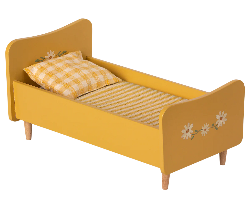 The Maileg Wooden Bed, Mini is a charming toddler bed in yellow, featuring hand-painted floral decorations on both the headboard and footboard. This delightful piece comes with a checked pillow and a striped blanket and is supported by four sturdy wooden legs, making it an enchanting choice for any child's room.