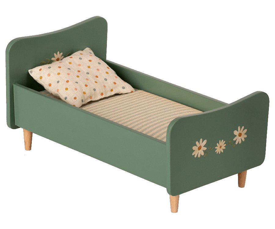 A small green wooden Maileg Wooden Bed, Mini with handpainted floral decorations and charming bunnies on the headboard and footboard. The bed has a beige mattress with thin stripes and a white pillow with brown polka dots. It stands gracefully on four short wooden legs.