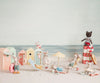 Stuffed toy mice lounge by beach huts with fun accessories, while a stuffed cat sits on boxes with a lifebuoy. The scene features the Maileg Rubber Boat, Small Mouse - Red Stripe, perfect for seaside summer adventures.