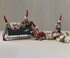 Four mini pixies with red hats and handpainted details arrange wrapped gifts and cookies around the Maileg Christmas Sleigh, Large - Green; some place items inside while others stand nearby on a light surface with a neutral background.