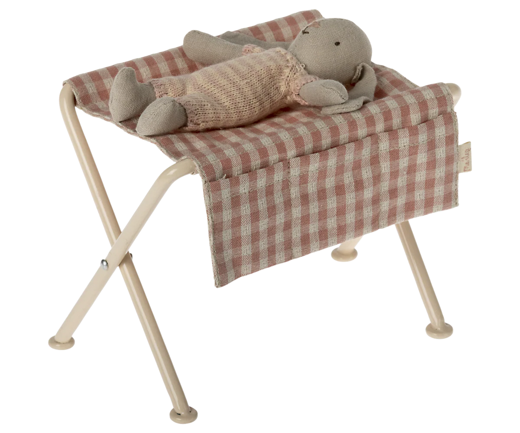 Maileg Nursery Table, Micro - Red Checker with a pink and white checkered seat is shown holding a stuffed rabbit doll in pink knit clothes, resembling cute baby furniture against a plain background.