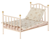 The Maileg Little Sister Bedroom Starter Set includes a small, vintage-style metal bed frame with gold accents, perfect for collectors. It comes with a floral-patterned pillow and mattress. The light-colored bedding features a subtle design, creating a quaint and cozy look.