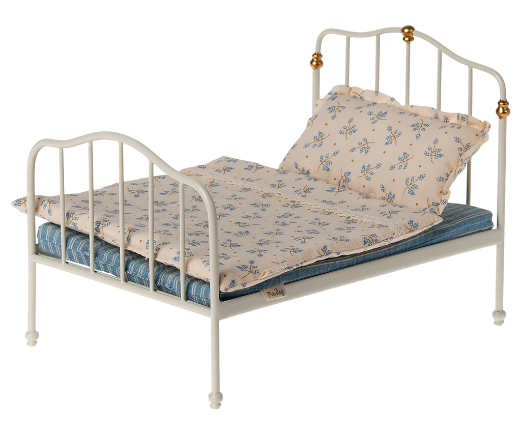 A charming Maileg Set - Sleepover At Grandparents features a small metal-framed doll bed with a white finish and elegant gold accents on the headboard. This delightful set includes a blue mattress dressed with a cream-colored blanket adorned with floral patterns and a matching pillow, perfect for Grandparents Mice to enjoy imaginative play.