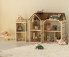 Two wooden dollhouses, including the charming Maileg Farmhouse Dollhouse, with miniature furniture and toy mice are arranged on a white rug. Nearby, a small toy car and a toy pig in a stroller add to the cozy, playful atmosphere, evoking a delightful mouse dollhouse world.