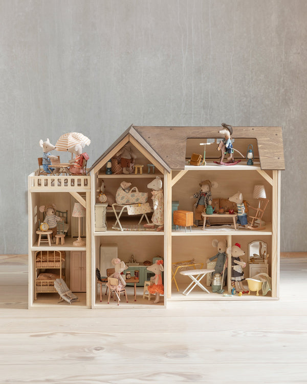 The Maileg Farmhouse Dollhouse, set against a neutral wall background, is adorned with tiny mouse figurines placed in various rooms, each thoughtfully decorated with miniature furniture and charming household items.