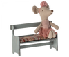 A fabric mouse doll wearing a pink ballet outfit, including a tutu and headband, is sitting on a small wooden bench with a striped cushion seat. The Maileg Christmas Mini Bench, part of the mouse family’s cherished collection, boasts a vintage look with its distressed light blue paint.