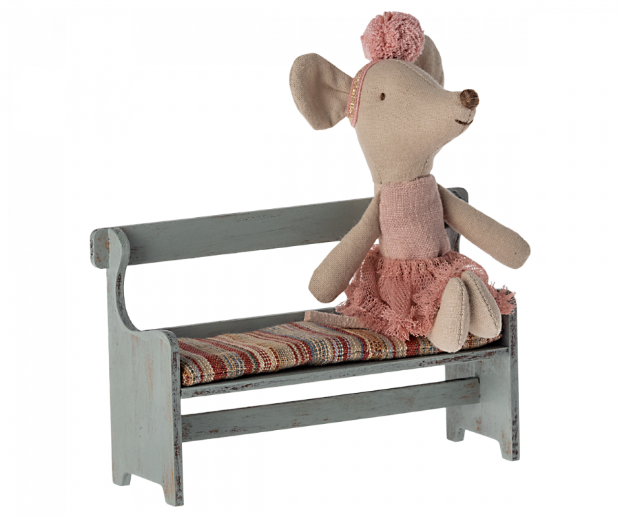 A fabric mouse doll wearing a pink ballet outfit, including a tutu and headband, is sitting on a small wooden bench with a striped cushion seat. The Maileg Christmas Mini Bench, part of the mouse family’s cherished collection, boasts a vintage look with its distressed light blue paint.