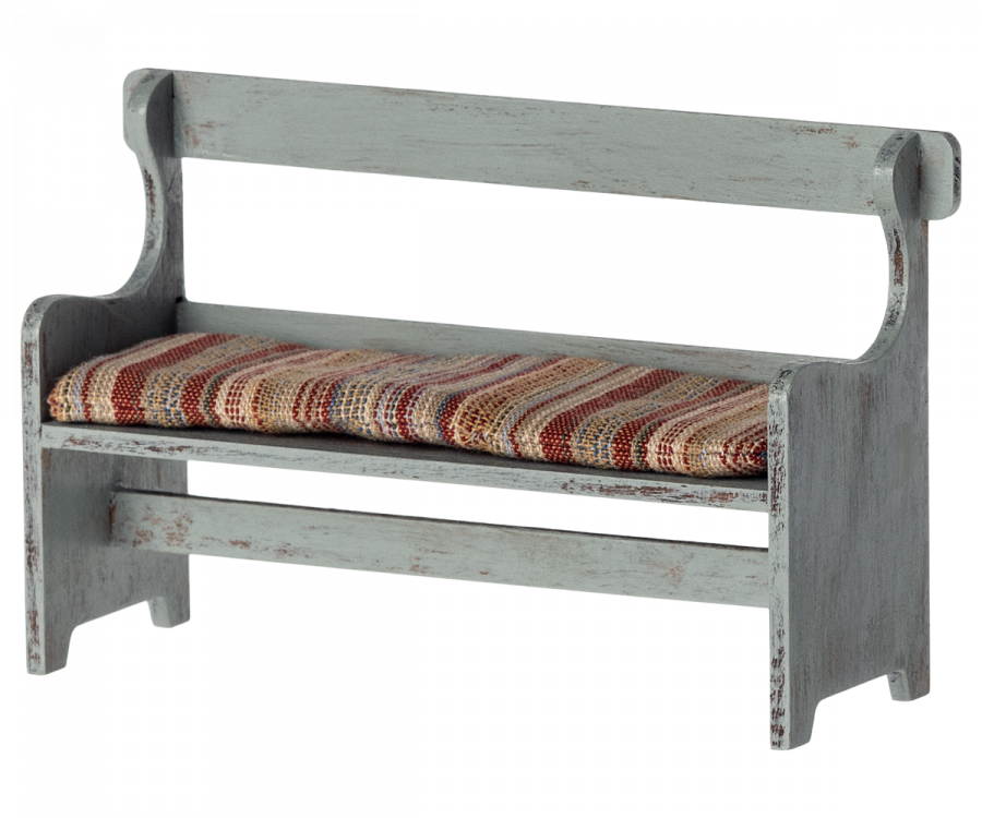 A small, rustic Maileg Christmas Mini Bench with a vintage look and a distressed light gray finish. It has a simple backrest and armrests with a striped cushion in shades of red, brown, and beige on the seat.