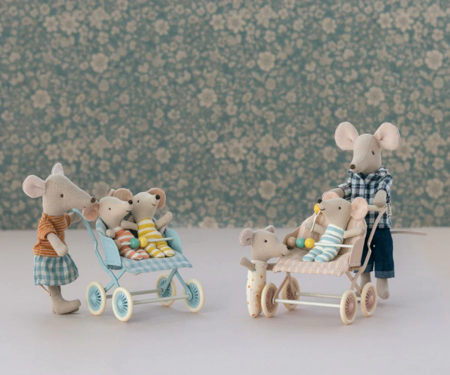 A family of stuffed mouse figures, with parents pushing strollers and transporting babies inside the Maileg Stroller, Baby Mice - Mint. The scene includes two groups; one parent is pushing a stroller holding two baby mice, while another group has a mouse parent pushing a Maileg Stroller, Baby Mice - Mint with a baby mouse and another small mouse standing by. The backdrop has soft blue floral wallpaper.