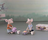 Two toy mice having a tea party, one pouring tea from a purple teapot and the other holding a cup, with a plate of pastries and a Maileg Miniature Afternoon Treat Tea Set - Purple Madelaine nearby, against a
