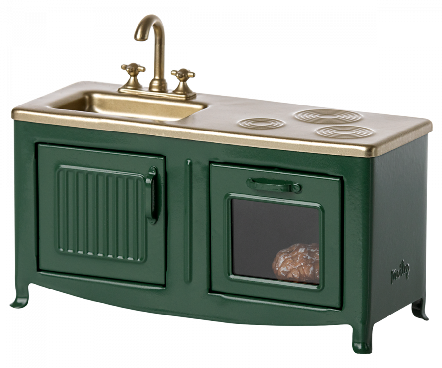 A Maileg Kitchen - Dark Green unit with a sink, faucet, and stove top, featuring gold accents and an oven door slightly ajar showing a loaf of bread inside.