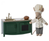 A plush mouse chef in a white chef's hat and jacket stands beside a Maileg Kitchen - Dark Green, holding a small whisk and presenting a freshly baked pie.