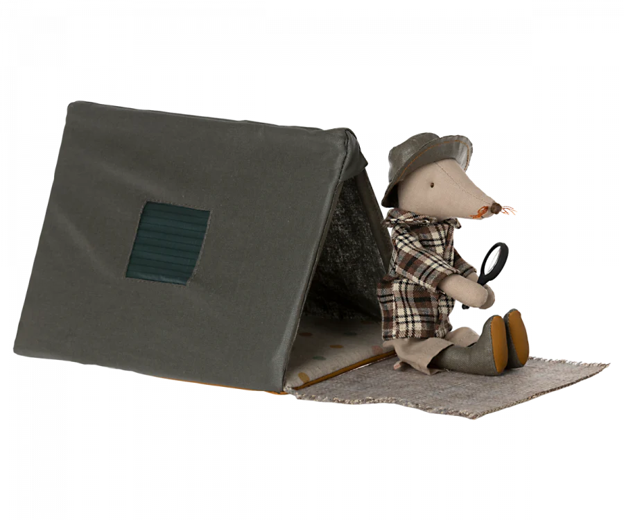 A Maileg mouse wearing a plaid shirt and detective hat, holding a magnifying glass, is near a Maileg Single Tent, Mouse Size on a textured surface, suggesting an adventure or investigation theme.