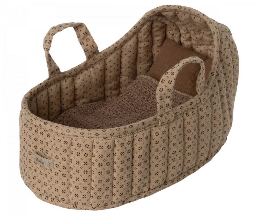 The Maileg Carry Cot, Large - Sand is a cozy and quilted portable bed adorned with a subtle brown floral pattern and equipped with handles for effortless carrying. Inside, it includes a neatly folded, brown knitted blanket that enhances both warmth and style.