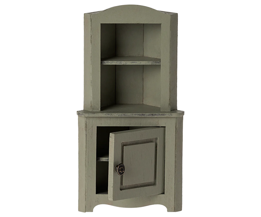 The Maileg Corner Cabinet, Mouse in Light Green is a small rustic wooden corner cabinet featuring an upper open shelf and a lower section with a closed door. The cabinet has a vintage finish that enhances its charm for home decoration. The partially open door reveals additional storage space inside.